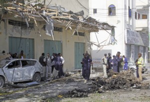 Somali soldiers stand near the wreckage after a car bomb detonated in Mogadishu, Somalia, Saturday, Dec. 19, 2015.  A Somali police officer says two people were killed and others were injured after a car bomb parked outside the shopping centre was detonated. (AP Photo/Farah Abdi Warsameh)